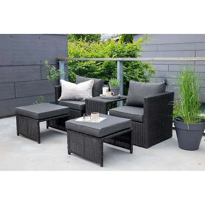 Ebuy24 Loungemöbel-Set Quad - 5 -tlg., Korbmöbel, Schwarz - Dunkelgraue Rattan-Gartenmöbelgarnitur mit grauen Kissen, bestehend aus zwei Stühlen, zwei Hockern und einem Beistelltisch auf einer Terrasse.
