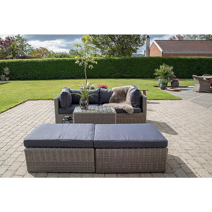 Ebuy24 Loungemöbel-Set Rosino - 3 -tlg., Polyrattan, Aluminium, Glas, Polyester, Grau - Graue Korbmöbel-Gartenlounge mit dunklen Kissen auf einer gepflasterten Terrasse.
