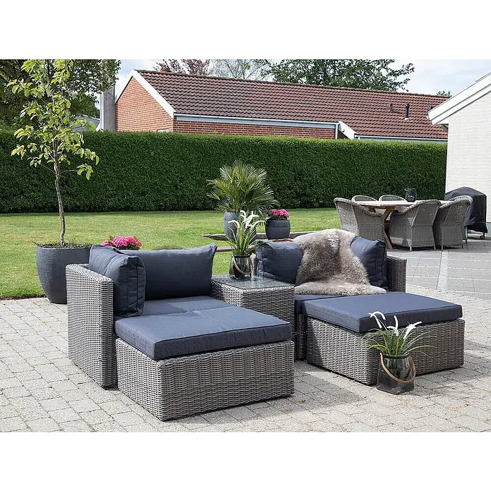 Ebuy24 Loungemöbel-Set Rosino - 3 -tlg., Polyrattan, Aluminium, Glas, Polyester, Grau - Graues Polyrattan-Loungeset mit dunkelblauen Kissen auf einer gepflasterten Terrasse im Garten.