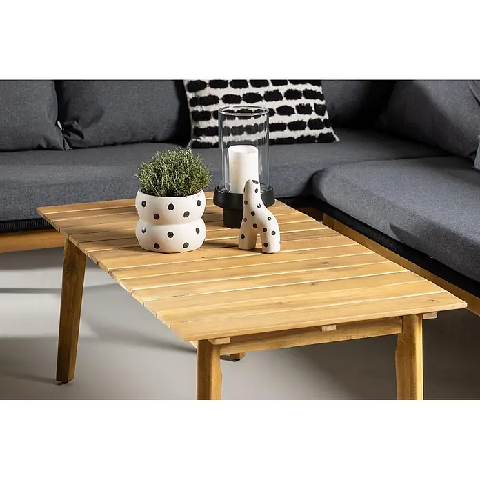 Ebuy24 Loungemöbel-Set Chania - 2 -tlg., Akazie, Schwarz - Heller Couchtisch aus Holzlatten mit Pflanzen und Deko vor einem grauen Sofa, schafft einen gemütlichen Sitzbereich.