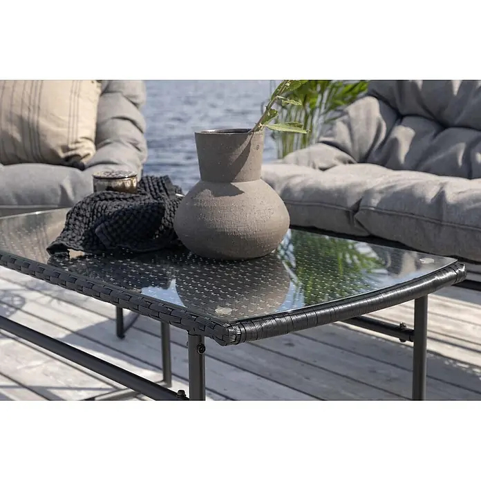Ebuy24 Loungemöbel-Set Tina - 4 -tlg., Stahl, Schwarz - Schwarzer Rattan-Couchtisch mit Glasplatte, auf Holzterrasse mit Sitzmöbeln im Freien.