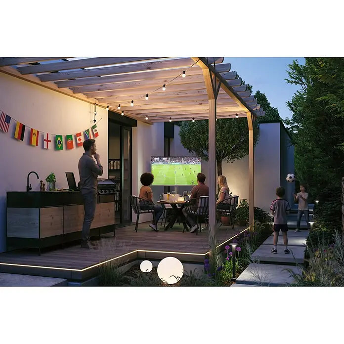 Paulmann Plug & Shine LED-Lichterkette - Außen, Lichtfarbe: Warmweiß, Anzahl Leuchtmittel: 7 Stk. - Eine Außenterrasse mit Pergola, großem Fernseher, der Fußball zeigt, und Gartenbeleuchtung, wo Menschen das Spiel genießen und Kontakte knüpfen.