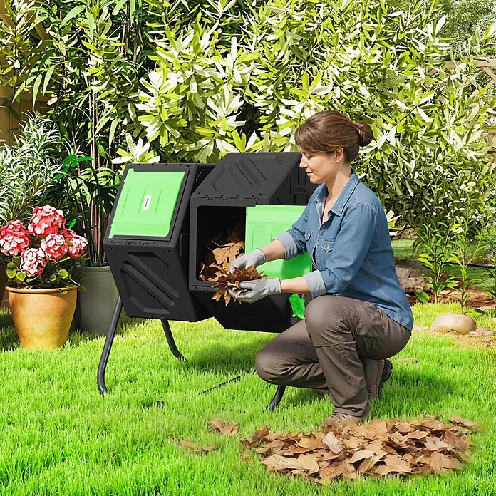 Outsunny Komposter - 130 l, 67 x 60 x 77 cm - Eine Frau fügt trockenes Laub in einen schwarz-grünen Drehkomposter im Garten.