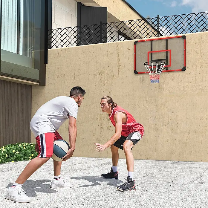 Sportnow Basketballkorb - Stahl, Schwarz, Transparent, Rot - Wandmontierter Basketballkorb mit transparenter Platte, rotem Rahmen und schwarzem Ring, genutzt von zwei Spielern auf einem Hof.