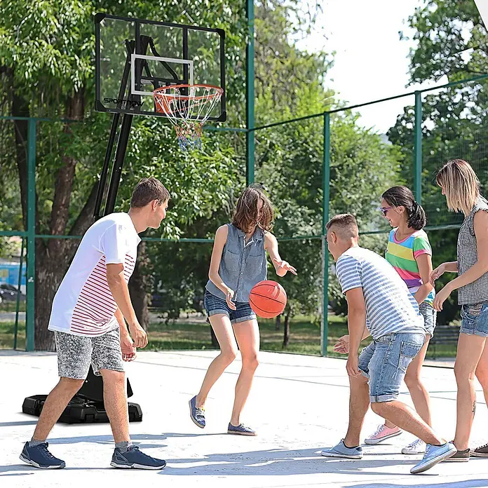 Sportnow Basketballkorb - Stahl, Schwarz - Schwarzer mobiler Basketballkorb mit klarer Platte und orangefarbenem Ring, wird von jungen Erwachsenen im Freien genutzt.