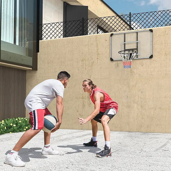 Sportnow Basketballkorb - Stahl, Schwarz, Transparent, Weiß - Wandmontierter Basketballkorb mit transparenter Platte, schwarzem Rahmen und rot-blauem Netz, von zwei Spielern im Freien genutzt.