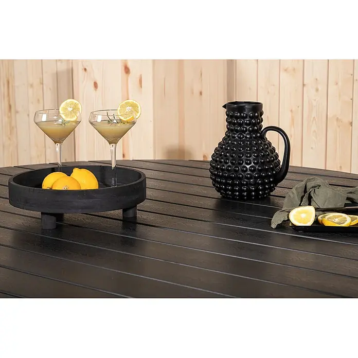 Ebuy24 Gartentisch rund Break - Ø x H: 150 x 74 cm, Aluminium, Schwarz, Stapelbar - Schwarzer Lamellentisch mit zwei Zitronen-Cocktails, einem strukturierten schwarzen Krug und frischen Zitronen.