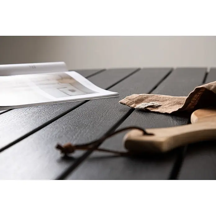 Ebuy24 Gartentisch rund Break - Ø x H: 120 x 74 cm, Aluminium, Schwarz, Stapelbar - Dunkelgrauer Lamellentisch mit texturierter Oberfläche, auf dem eine Zeitschrift, ein zerknittertes Tuch und ein Holzbrett liegen.