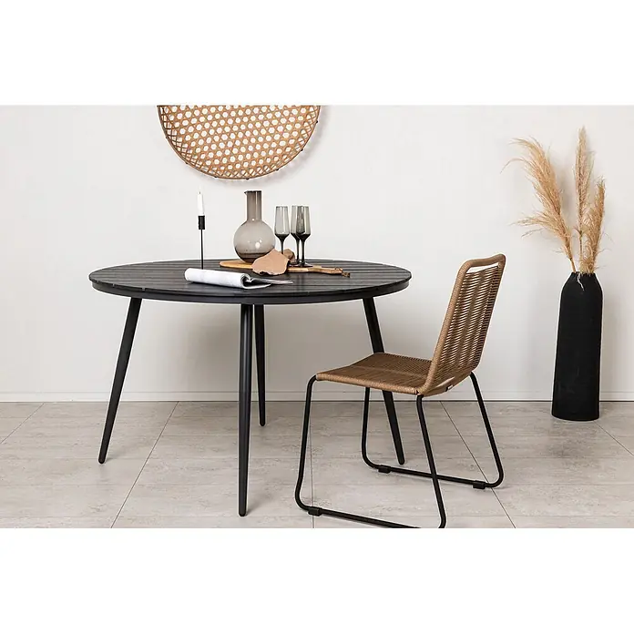Ebuy24 Gartentisch rund Break - Ø x H: 120 x 74 cm, Aluminium, Schwarz, Stapelbar - Dunkler runder Lamellen-Esstisch mit schwarzen Beinen und brauner geflochtener Stuhl mit schwarzem Gestell in einem Raum.