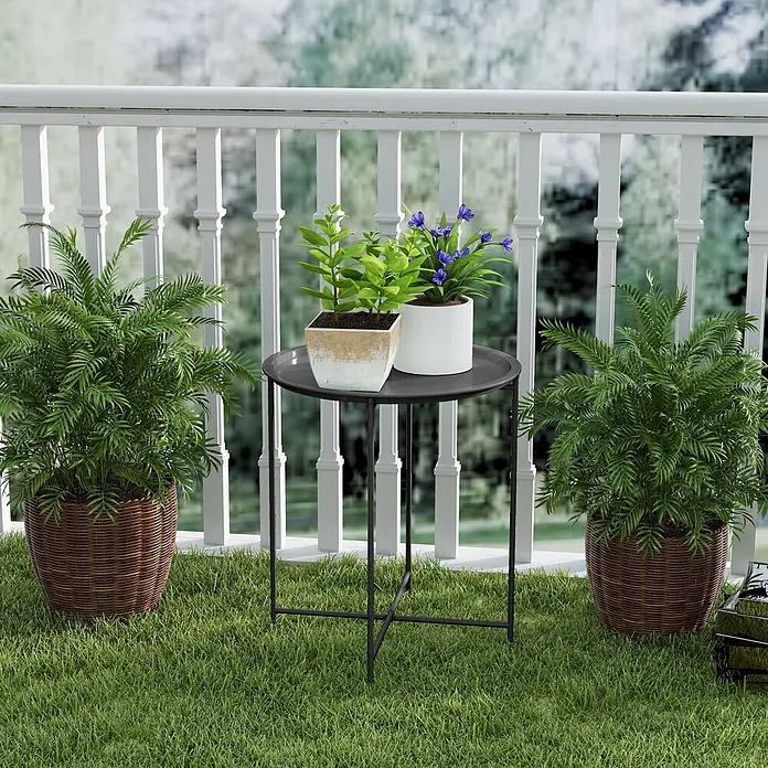 Outsunny Garten-Beistelltisch rund - Stahl, Schwarz - Runder schwarzer Beistelltisch aus Metall auf grasbewachsenem Balkon, mit zwei Topfpflanzen.