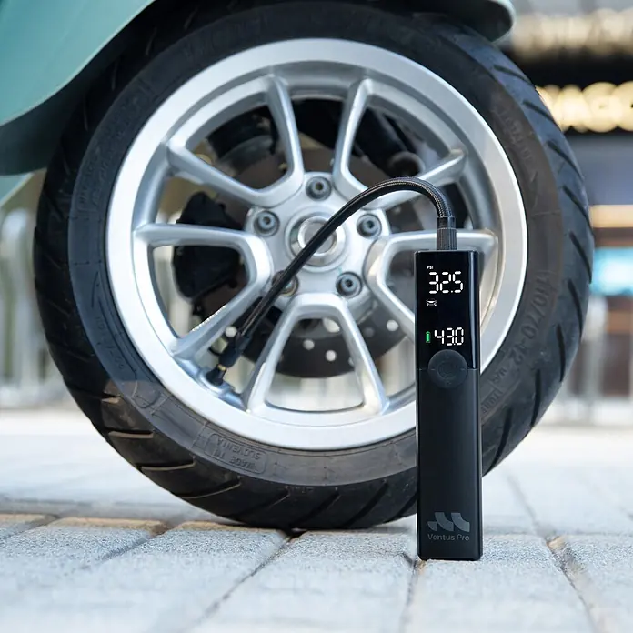 Mini bomba de aire Woowind Ventus Pro - 7,4 V, 10,34 bar, Capacidad de bombeo máx.: 22 l/h - Bomba de aire portátil negra Ventus Pro con pantalla digital de PSI y batería, conectada a un neumático de scooter para inflar.