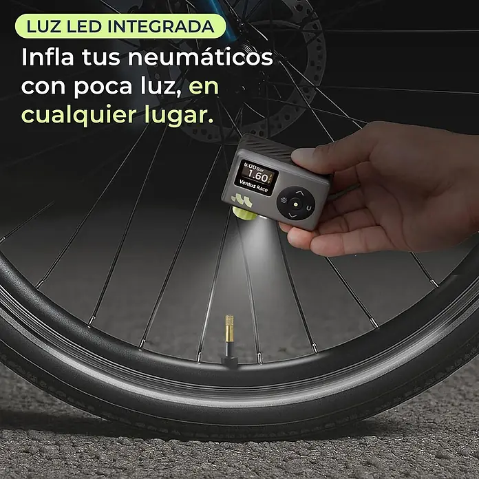 Mini bomba de aire Woowind Ventus Race - 7,4 V, 8,27 bar, Capacidad de bombeo máx.: 14 l/h - Una mano sostiene un inflador de neumáticos gris con luz LED integrada, iluminando la válvula de una bicicleta en la oscuridad.