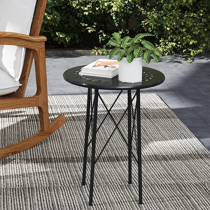 Outsunny Garten-Beistelltisch rund - Stahl, Schwarz - Schwarzer Metall-Beistelltisch mit perforierter Platte, im Freien neben einem Schaukelstuhl auf einem Teppich.