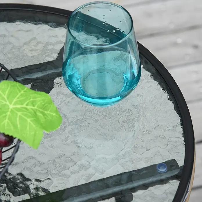 Outsunny Garten-Beistelltisch rund - Ø x H: 45 x 50 cm, Metall, Glas, Schwarz - Ein leuchtend blaugrünes Glas mit Wassertropfen auf einem strukturierten Glastisch im Freien.