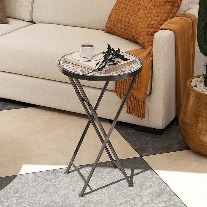 Outsunny Garten-Beistelltisch rund - Ø x H: 35,5 x 55 cm, Metall, Keramik, Mehrfarbig - Ein runder klappbarer Beistelltisch mit bunter Mosaikplatte und dunklen Metallbeinen, neben einem cremefarbenen Sofa, mit Tasse, Buch und Pflanze.