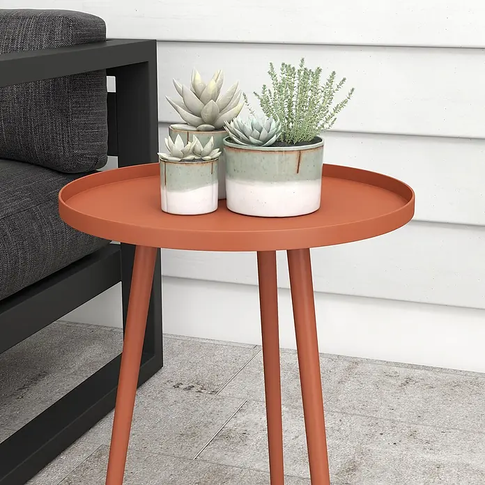 Outsunny Garten-Beistelltisch rund - Ø x H: 40 x 50 cm, Stahl, Rot - Ein oranger runder Beistelltisch mit drei Beinen, darauf drei Topfpflanzen, neben einem dunkelgrauen Outdoor-Sofa.