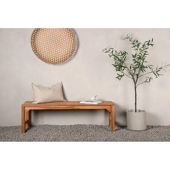Ebuy24 Gartenbank Kenya - B x T x H: 150 x 150 x 45 cm, Teak, Holz - Holzbank mit beigem Kissen, Tasse und Buch, in einem minimalistischen Raum mit Olivenbaum.