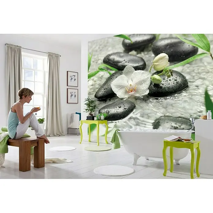 Komar Fototapete Pure - 8 -tlg., B x H: 368 x 254 cm, Papier - Entspannendes Badezimmer-Interieur mit einer Frau, die auf einem Holzhocker sitzt, und einer Stein- und Orchideenwand.