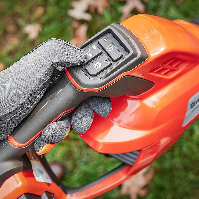 Husqvarna Akku-Laubbläser 230iB - 1 Akku, Blasgeschwindigkeit: 220 km/h - Behandschuhte Hand bedient orange-dunkelgraues Gartengerät mit Geschwindigkeits- und Leistungstasten.