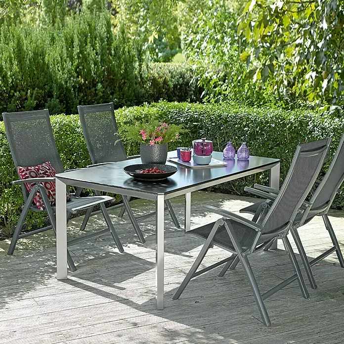 Sunfun Maja Sillón de posiciones - 61 x 68 x 110 cm, Antracita, Aluminio/Textiline - Mesa de jardín con cuatro sillas en una terraza de madera, rodeada de exuberante vegetación. El conjunto es ideal para relajarse al aire libre.