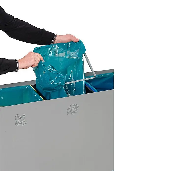 Proregal Wertstoffsammler robust mit 3 Einsätzen - 89 l - Eine Person legt einen blauen Müllsack in einen grauen Mehrkammer-Recyclingbehälter mit Mülltrennsymbolen auf der Vorderseite.