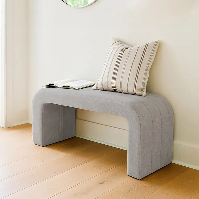 Banco Tapizado - L x An x Al: 76 x 38 x 45 cm, Madera, Gris - Banco curvo tapizado gris claro con un libro y cojín a rayas.