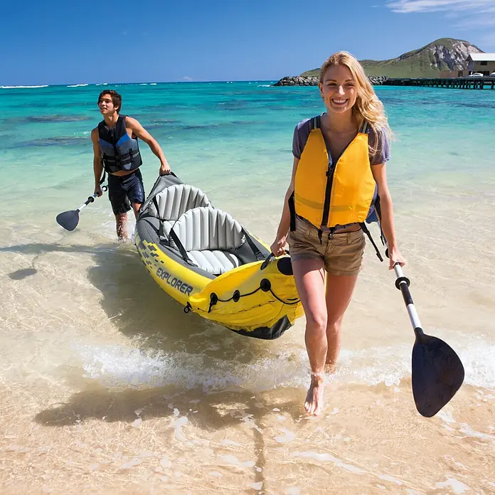 Intex Kajak Explorer K2 - 313 x 92 cm, Nutzlast: 160 kg, Geeignet für: 2 Personen - Gelbes Schlauchkajak 'EXPLORER' wird von zwei Personen in klares flaches Wasser am Strand getragen.