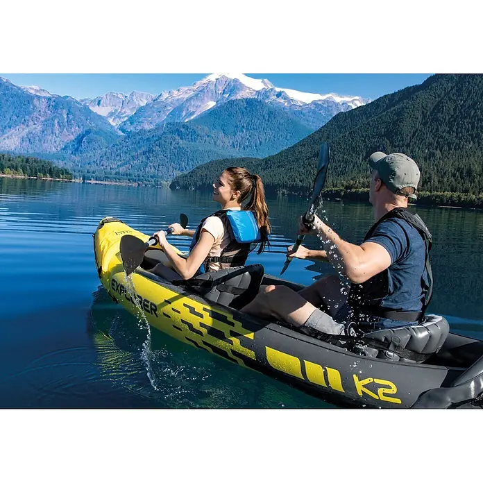 Intex Kajak Explorer K2 - 313 x 92 cm, Nutzlast: 160 kg, Geeignet für: 2 Personen - Zwei Personen paddeln in einem gelb-grauen Schlauchkajak auf einem See, umgeben von Bergen.