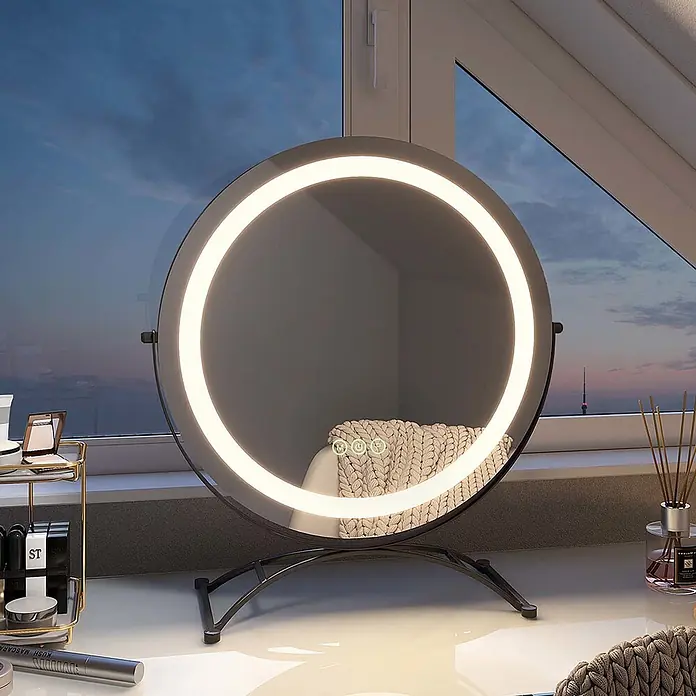 Emke Kosmetikspiegel CM07 - 40 x 47 cm, Rund, Schwarz - Runder LED-Schminkspiegel mit schwarzem Standfuß auf weißem Tisch, reflektiert eine gestrickte Decke. Fensterblick im Hintergrund.