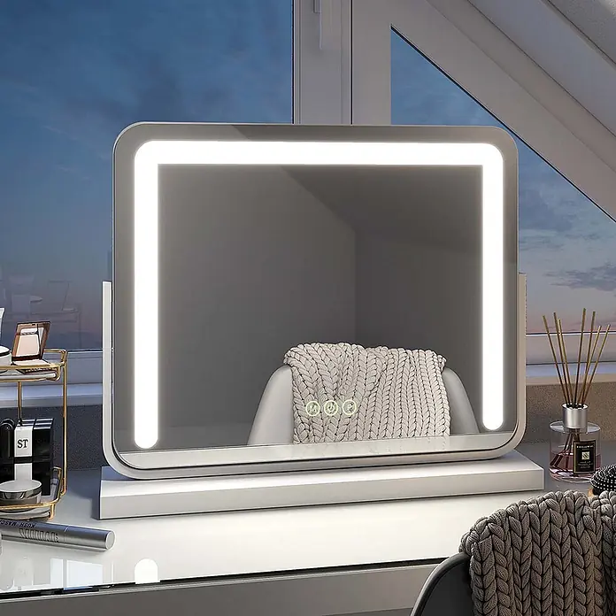Emke Kosmetikspiegel Glozia - 50 x 41,6 cm, Rechteckig, Weiß - Weißer LED-Kosmetikspiegel mit integrierten Lichtern und Touch-Bedienelementen, der ein gemütliches Interieur widerspiegelt. Steht auf einem Schminktisch.