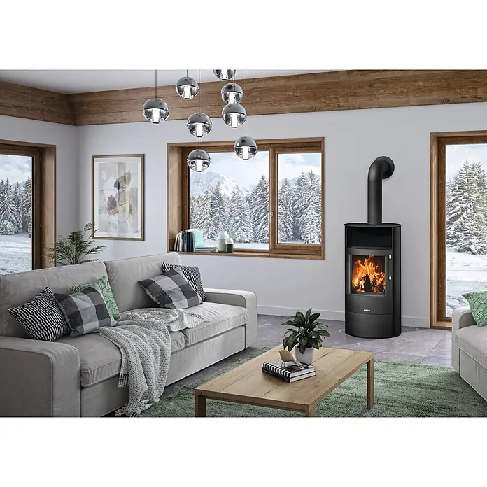 Justus Kaminofen Island 7 2.0 - 7 kW, Raumheizvermögen: 144 m³, Farbe Verkleidung: Schwarz - Ein eleganter schwarzer Holzofen mit sichtbaren Flammen in einem gemütlichen Wohnzimmer, der Wärme und Atmosphäre spendet.