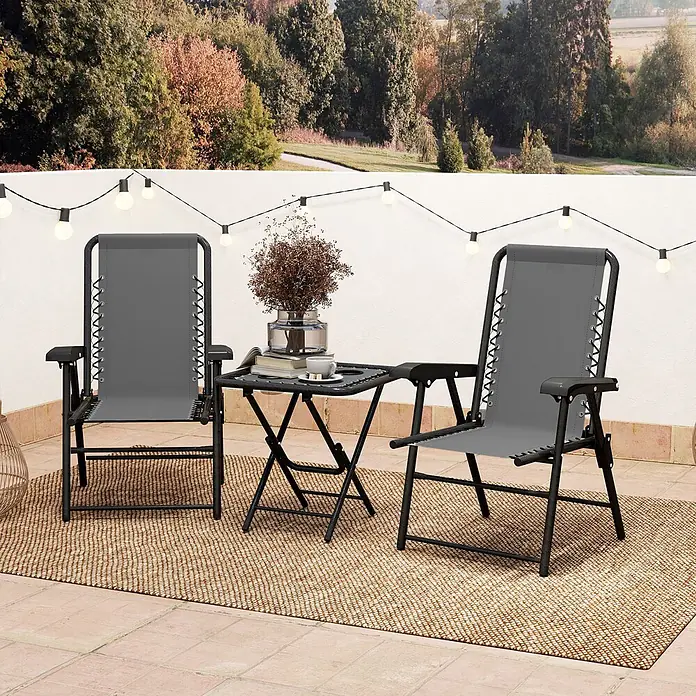 Outsunny Gartentisch-Set - Gesamtumfang: 3 -tlg., Stahl, Netzstoff, Klappbar - Zwei graue Schwerelosigkeitsliegen flankieren einen schwarzen Klapptisch auf einem Outdoor-Teppich, unter Lichterketten und vor Baumbewuchs.