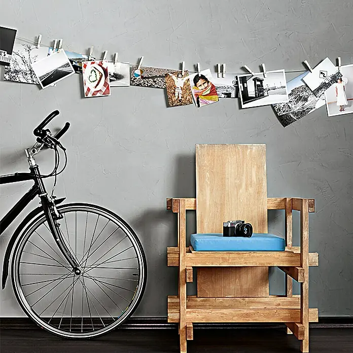 SCHÖNER WOHNEN-Farbe Trendstruktur Dekoputz-Set Beton-Optik - 5 -tlg., Grau - Dieses Bild zeigt einen Holzstuhl mit einem blauen Kissen, eine Kamera darauf, ein Fahrrad und eine Reihe von Fotos an der Wand.