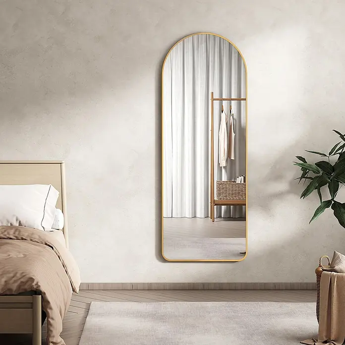 Emke Standspiegel FM07 - 60 x 160 cm, Glas - Ein gewölbter, goldgerahmter Ganzkörperspiegel lehnt im Schlafzimmer und reflektiert weiße Vorhänge und einen Kleiderständer.