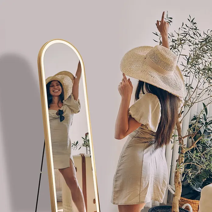 Emke Standspiegel FM06 - 45 x 147 cm, Glas - Goldgerahmter LED-Standspiegel, der eine Frau zeigt, die fröhlich ihr Spiegelbild betrachtet.