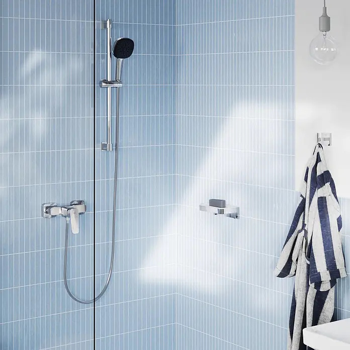 Grohe Dice Brausearmatur - Chrom, Glänzend - Verchromtes Duschset mit Handbrause, Seifenschale und Handtuchhaken in einer blau gefliesten Dusche.