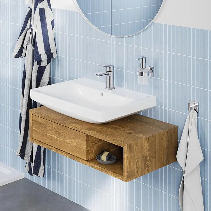 Grohe Dice Waschtischarmatur S-Size - Höhe: 152 mm, Chrom, Glänzend - Ein modernes Badezimmer mit weißem Keramikwaschbecken auf einem hellen, wandmontierten Holzwaschtisch mit Schublade vor blauen Fliesen.