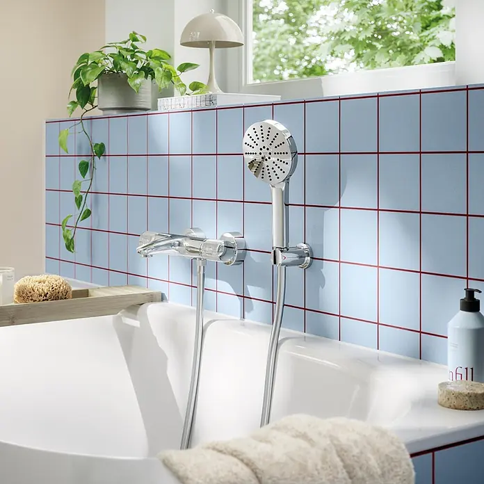 Grohe Vitalio Joy Handbrause 120 - Anzahl Funktionen: 3 Stk., Durchmesser: 120 mm, Chrom - Chrom-Duscharmatur und Handbrause über einer weißen Badewanne an blau-rot gefliester Wand montiert.