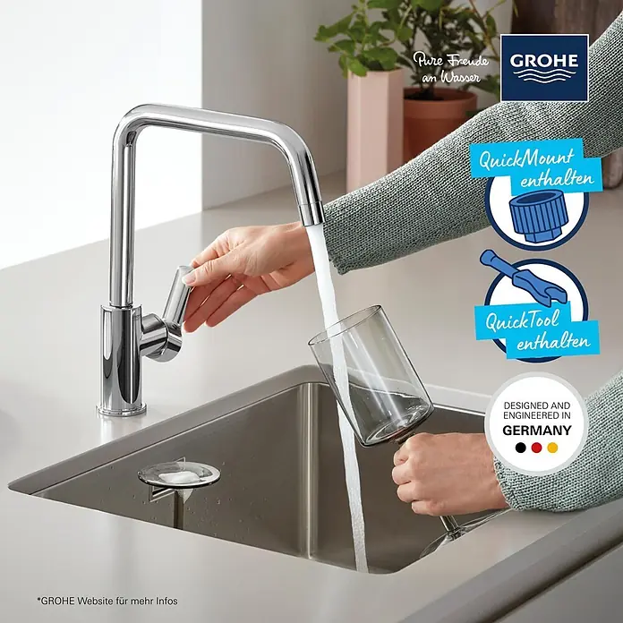 Grohe Start Spültischarmatur - Chrom, Glänzend - Verchromte Grohe Küchenarmatur in Edelstahlspüle, Wasser fließt in ein Glas, gehalten von Händen.