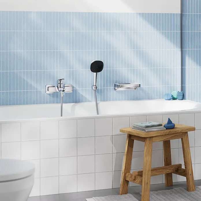 Grohe Dice Badewannenarmatur - Ausladung Armatur: 167 mm, Chrom, Glänzend - Helles Badezimmer mit weißer Badewanne, Chrom-Brausemischer und Handbrause sowie blau-weißen Fliesenwänden.