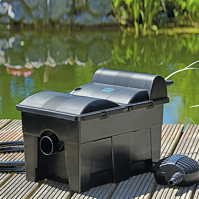 Oase BioSmart Durchlauffilter Set 14000 - 70 W, Teichgröße: 14 m³ - Ein schwarzer Teichfilter und eine Pumpe auf einem Holzsteg, vor einem Teich.