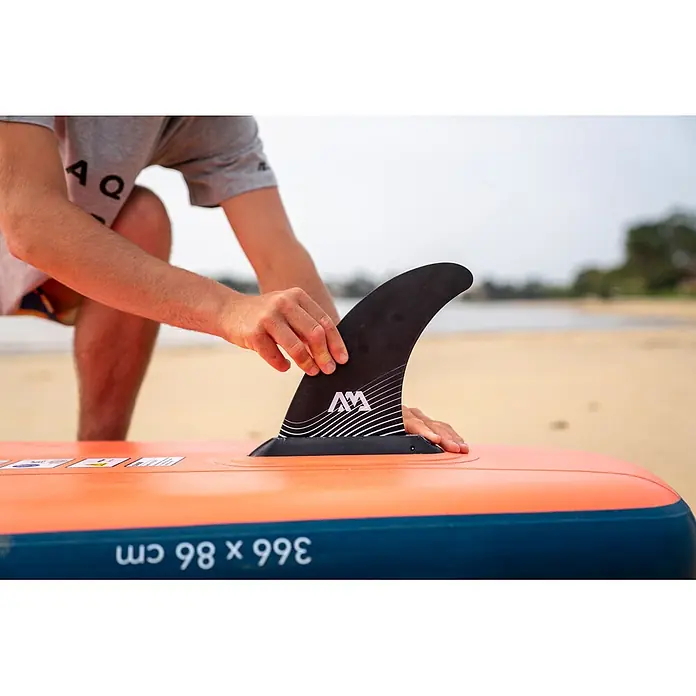 Aqua Marina SUP-Board-Set Atlas - L x B x H: 366 x 86 x 15 cm, Tragkraft: 180 kg, Orange - Person befestigt schwarze Finne mit weißem AM-Logo an orange-blauem Paddleboard am Strand.