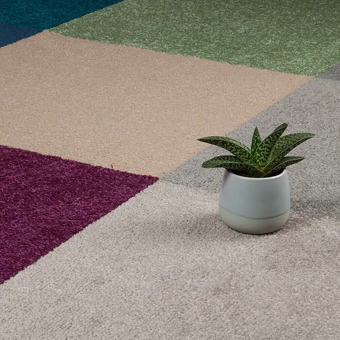 Bricoflor Teppichfliese Velours Hochflor, Creme Beige, 50 - Breite: 50 cm, Velours, 100 % Polypropylen (PP), Creme Beige - Ein flauschiger, mehrfarbiger Teppich mit geometrischem Muster und lebhaften Abschnitten, darauf eine kleine Topfpflanze.