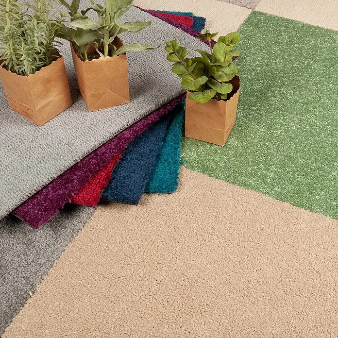 Bricoflor Teppichfliese Velours Hochflor, Beige Hell-Braun, 50 - Breite: 50 cm, Velours, 100 % Polypropylen (PP), Beige Hell-Braun - Texturierte Teppichmuster in verschiedenen Farben (Grau, Beige, Grün, Lila, Rot, Blau), präsentiert in einer Auslage mit kleinen Topfpflanzen.