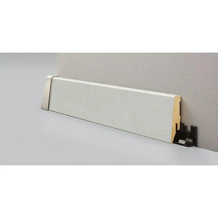 LOGOCLIC Sockelleiste K58 C Cremona - 260 cm x 18 mm x 58 mm, MDF - Nahaufnahme einer weißen Sockelleiste mit Montageclip, die an einer grauen Wand befestigt ist.