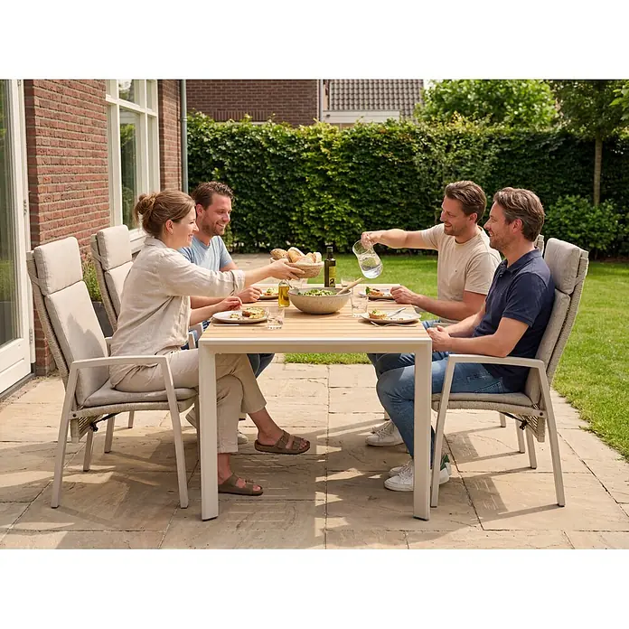 Barths Gartentisch Paros - L x B x H: 160 x 90 x 76 cm, Aluminium, Teak, Beige/Braun - Garten-Essgruppe: heller Tisch mit Lattenplatte, passende Stühle mit geflochtenen Details und Kissen. Leute essen auf einer Terrasse.