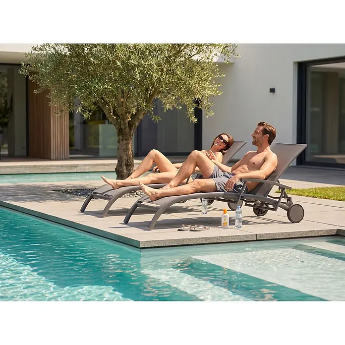 Barths Gartenliege Larino - B x T x H: 72 x 202 x 47 cm, Aluminium, Textilene, Anthrazit - Zwei graue Sonnenliegen mit Rollen am Pool, genutzt von einem Paar, das in der Sonne entspannt.