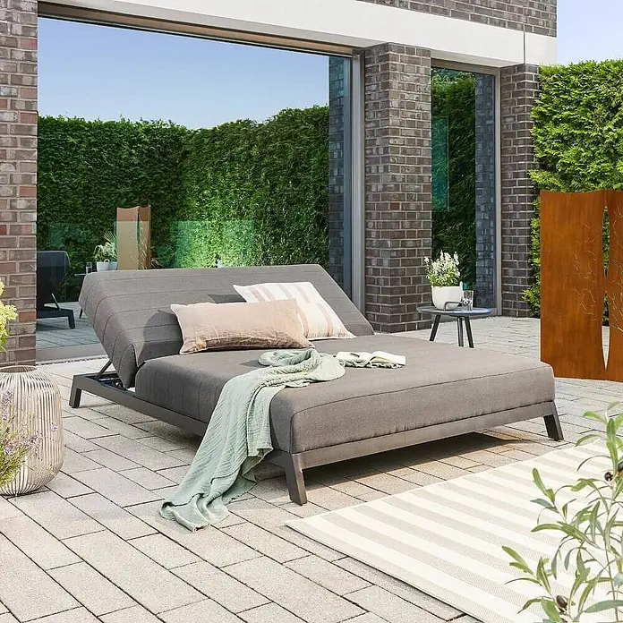 Home Deluxe Gartenliege VALENCIA - Grau, Sonstiges - Graues Garten-Tagesbett mit verstellbarer Rückenlehne und hellen Kissen, mit grünem Überwurf. Auf einer gepflasterten Terrasse.