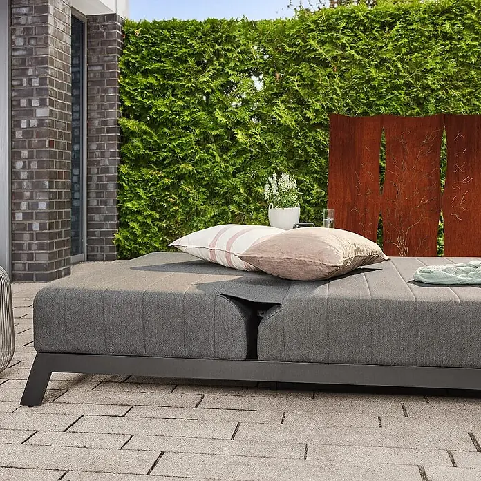 Home Deluxe Gartenliege VALENCIA - Grau, Sonstiges - Graues gepolstertes Outdoor-Daybed mit verstellbarer Rückenlehne und Kissen auf einer gepflasterten Terrasse.