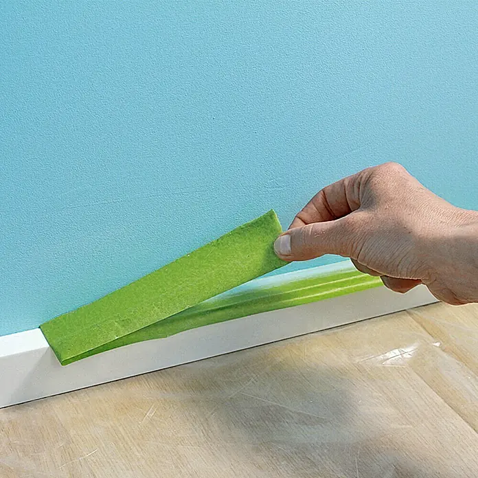 Frogtape Kreativklebeband Multi-Surface - 41,1 m x 36 mm, Grün, 1 -tlg. - Ein grünes Malerkreppband wird an einer weißen Fußleiste angebracht, um die Wand beim Streichen zu schützen. Ideal für saubere Farbkanten.